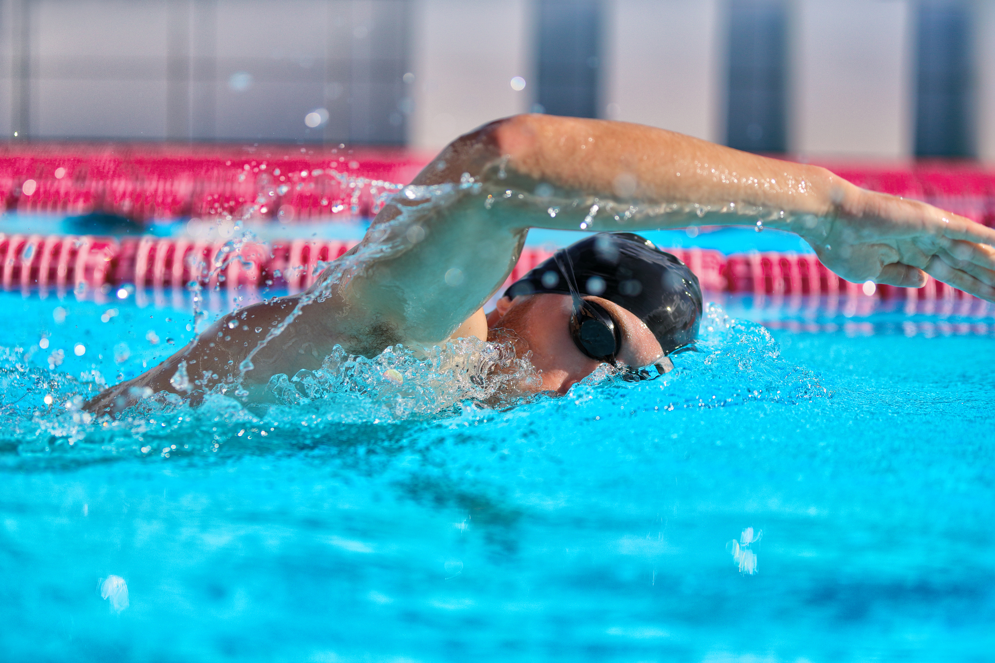 Swimmer man doing crawl swim in swimming pool portrait. Closeup of athlete wearing goggles, swimming cap training in blue water indoors